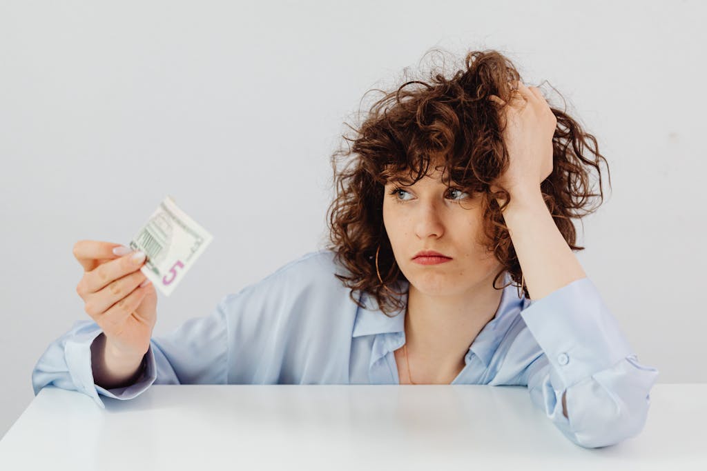 Concerned woman with curly hair holding a five dollar bill, expressing financial worry.