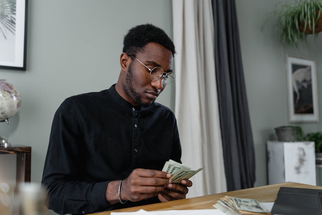 EOFY Checklist: 15 Things Every Aussie Should Do Before 30 June 2026 2 A focused man in glasses counting cash at a desk, indicating financial management.