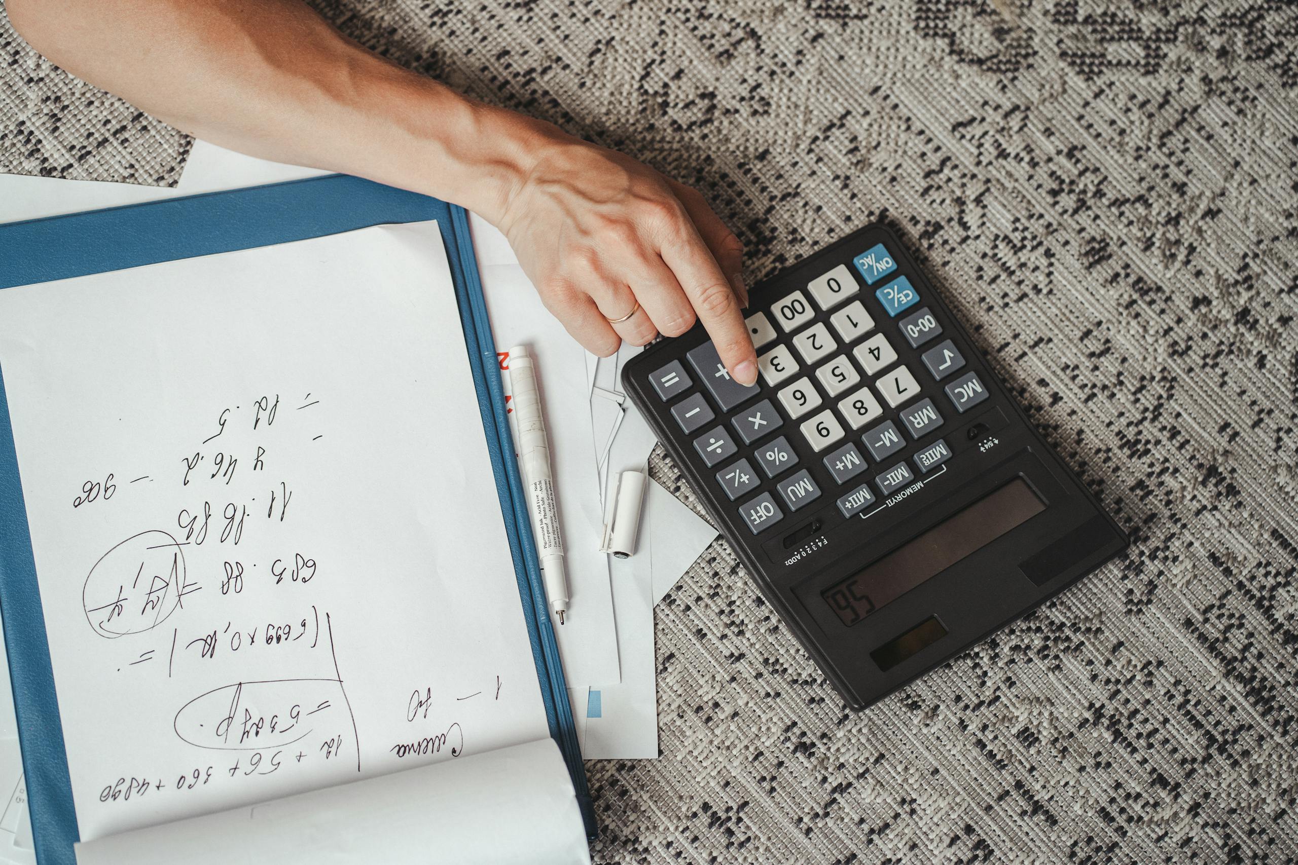 Fixed Rate vs Actual Cost: Home Office Deduction Guide 1 Top view of a hand calculating numbers with a large calculator and notes on a desk.